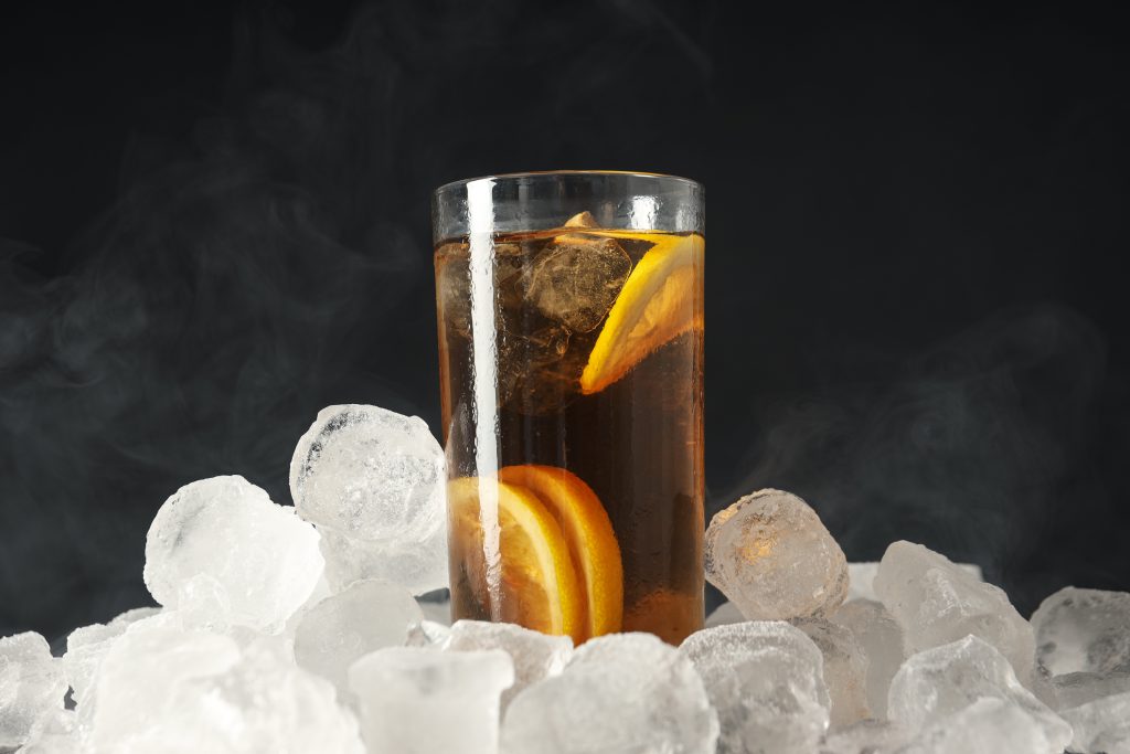 Glas mit Eistee und Orangenscheiben auf einem Berg von Eiswürfeln