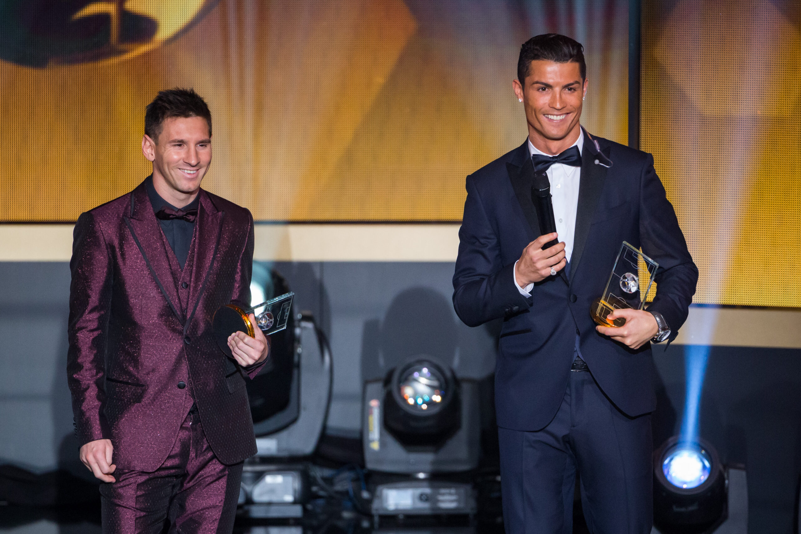 Ronaldo und Messi auf einer Bühne. Messi trägt einen bordeauxfarbenen und Ronaldo einen dunkelblauen Anzug