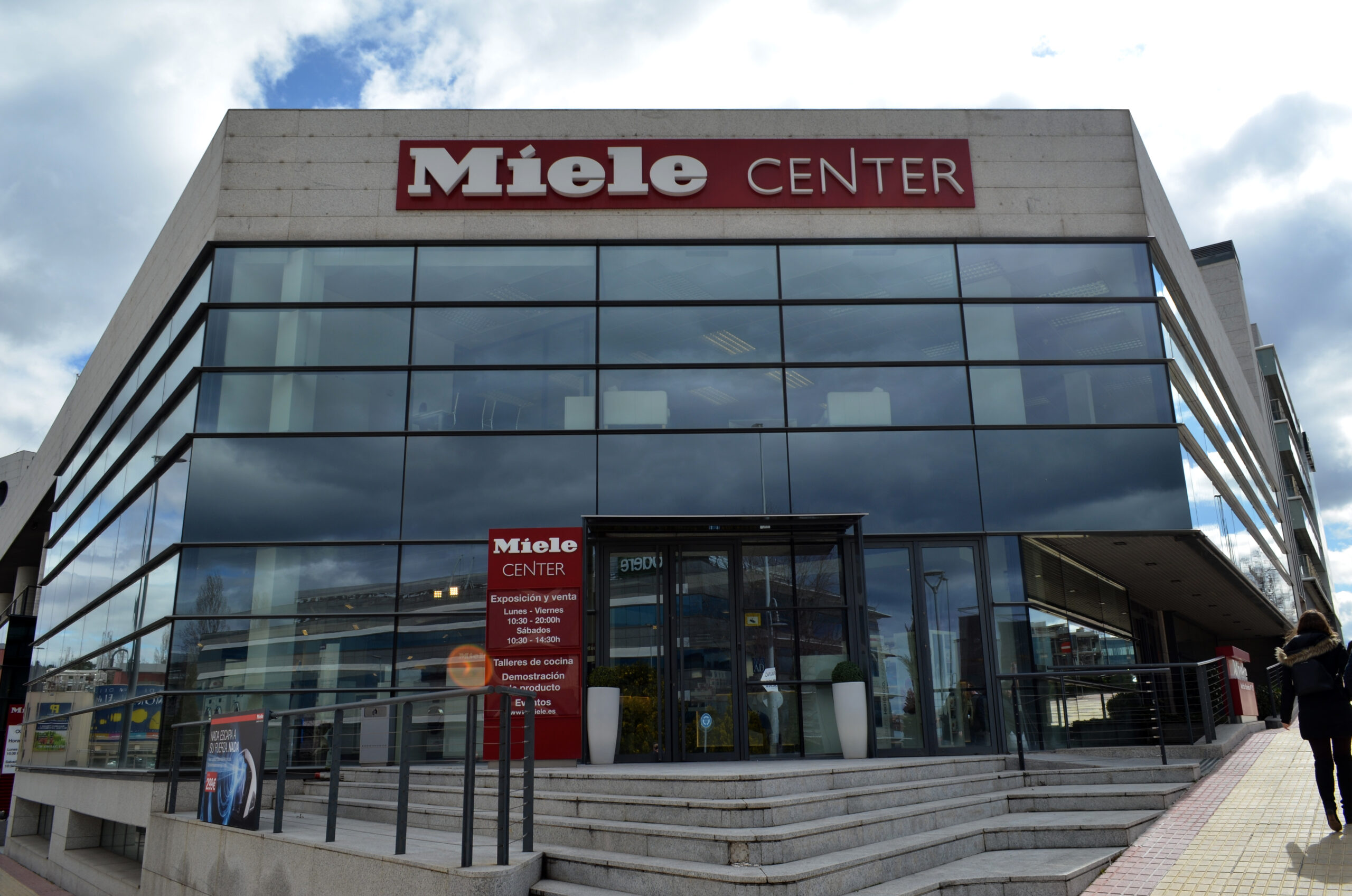 Firmengebäude von Miele mit dem Logo Miele Center in weißen Buchstaben auf rotem Hintergrund. Vor dem Eingang sind einige Stiegen