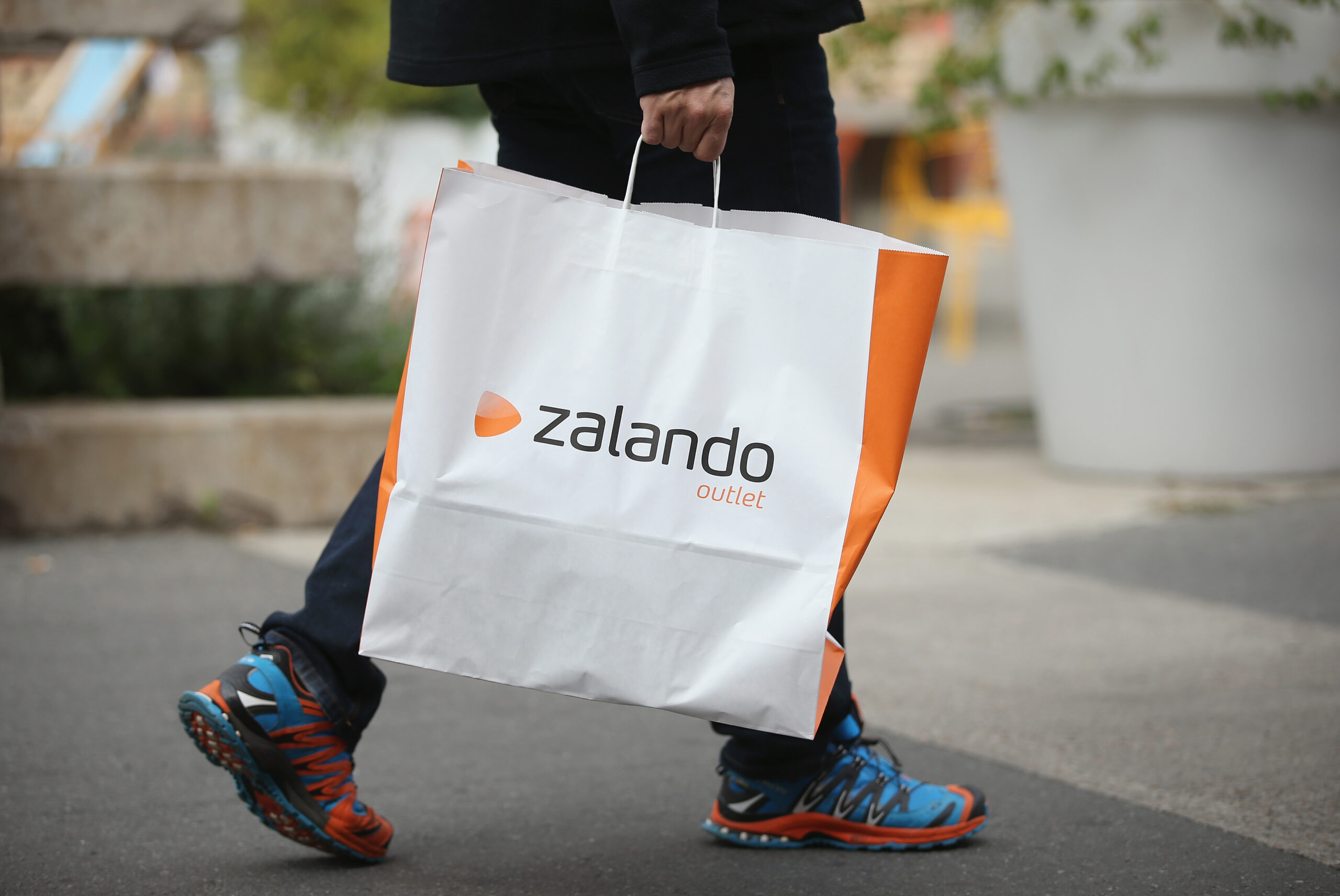 Zalando Einkaufstüte wird von einem Menschen mit Turnschuhen in blau und rot getragen