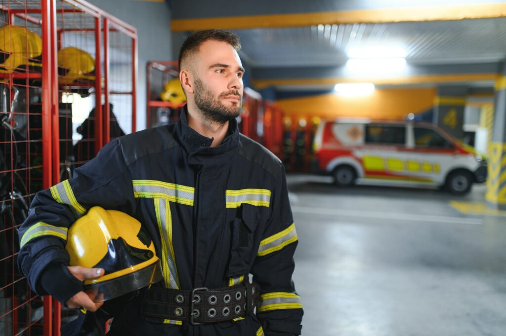 Feuerwehrmann mit Helm unter dem Arm eingeklemmt in einer Halle mit einem Feuerwehrauto