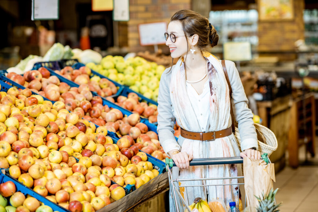 Frau mit einem Einkaufswagen steht neben Regalen gefüllt mit Äpfeln 