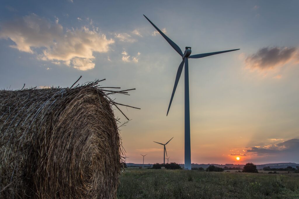 Strohballen und viele Windräder auf einem Feld. Dahinter ein Sonnenuntergang am Horizont