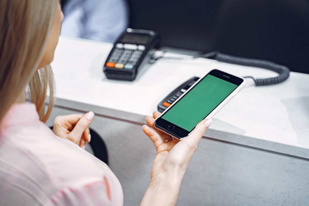 Frau hält ein Handy mit grünem Display auf einen Kassenautomaten