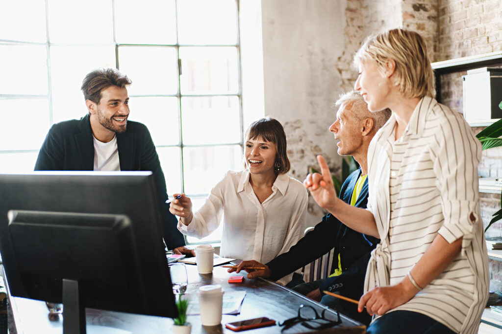 Vier Menschen sitzen vor einem PC und lachen gemeinsam