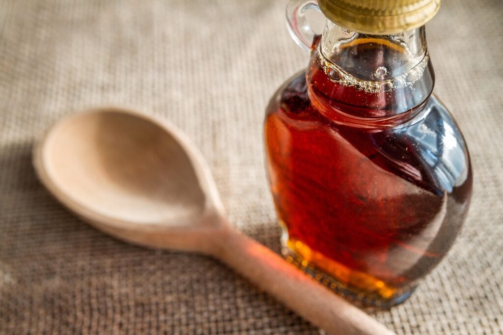 Eine Glasflasche mit Ahornsirup steht auf einer Holzarbeitsplatte, während sich die Frage nach dem künftigen Ahornsirup-Preis stellt – Foto: piviso / Pixabay