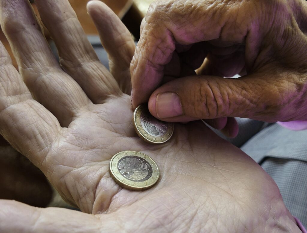 Eine Hand hält eine E-Card neben Euromünzen auf einem Tisch, sinnbildlich für den neuen Pension Abzug ab November – Foto: anaterate / Pixabay