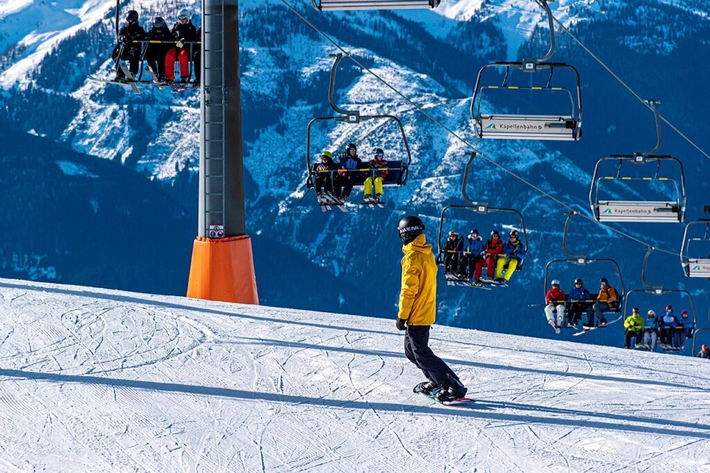 Eine Skisaisonkarte hängt an einem Jackenreißverschluss vor verschneiter Piste, während der Preis für die Skisaisonkarte diese Saison steigt – Foto: Ri_Ya / Pixabay