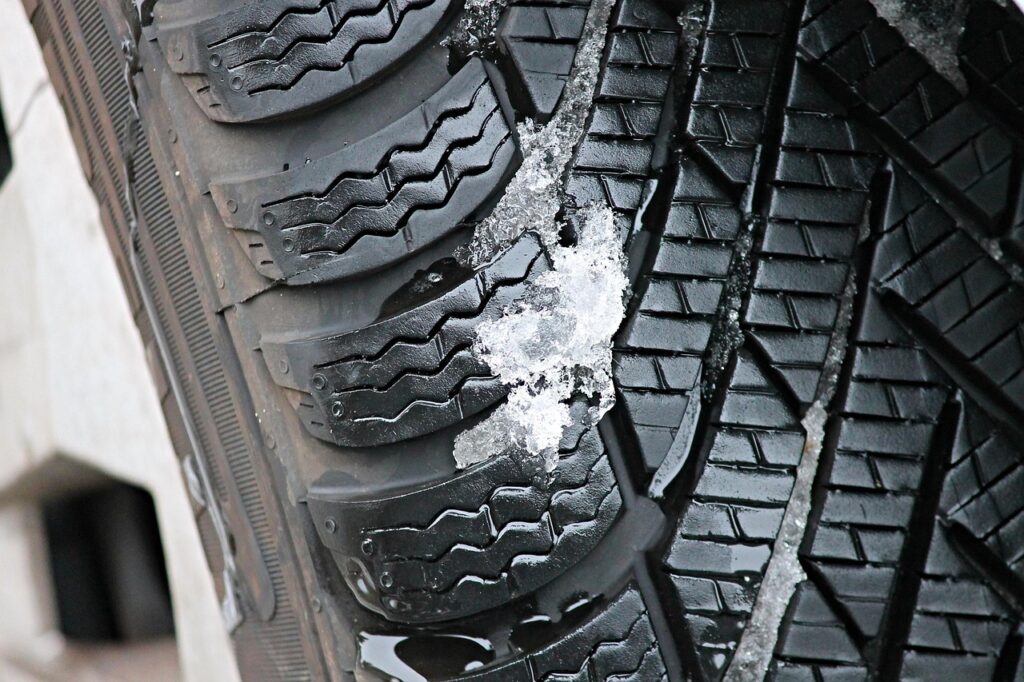 Ein neuer Winterreifen mit tiefem Profil lehnt in einer Werkstatt an einem Autorad, wie Autofahrer beim Winterreifen sparen können – Foto: manfredrichter / Pixabay