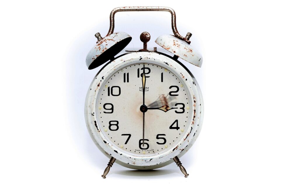 Ein analoger Wecker auf einem Nachttisch symbolisiert die Zeitumstellung im Oktober, bei der die Uhr eine Stunde zurückgestellt wird – Foto: PIRO4D / Pixabay