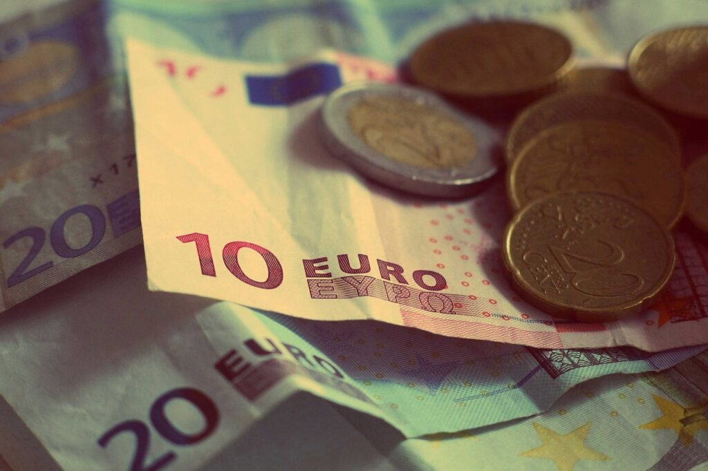 Münzen und Geldscheine auf einem Schreibtisch stehen sinnbildlich für den Streit um die Pflicht zur Betriebsrente – Foto: StockSnap / Pixabay